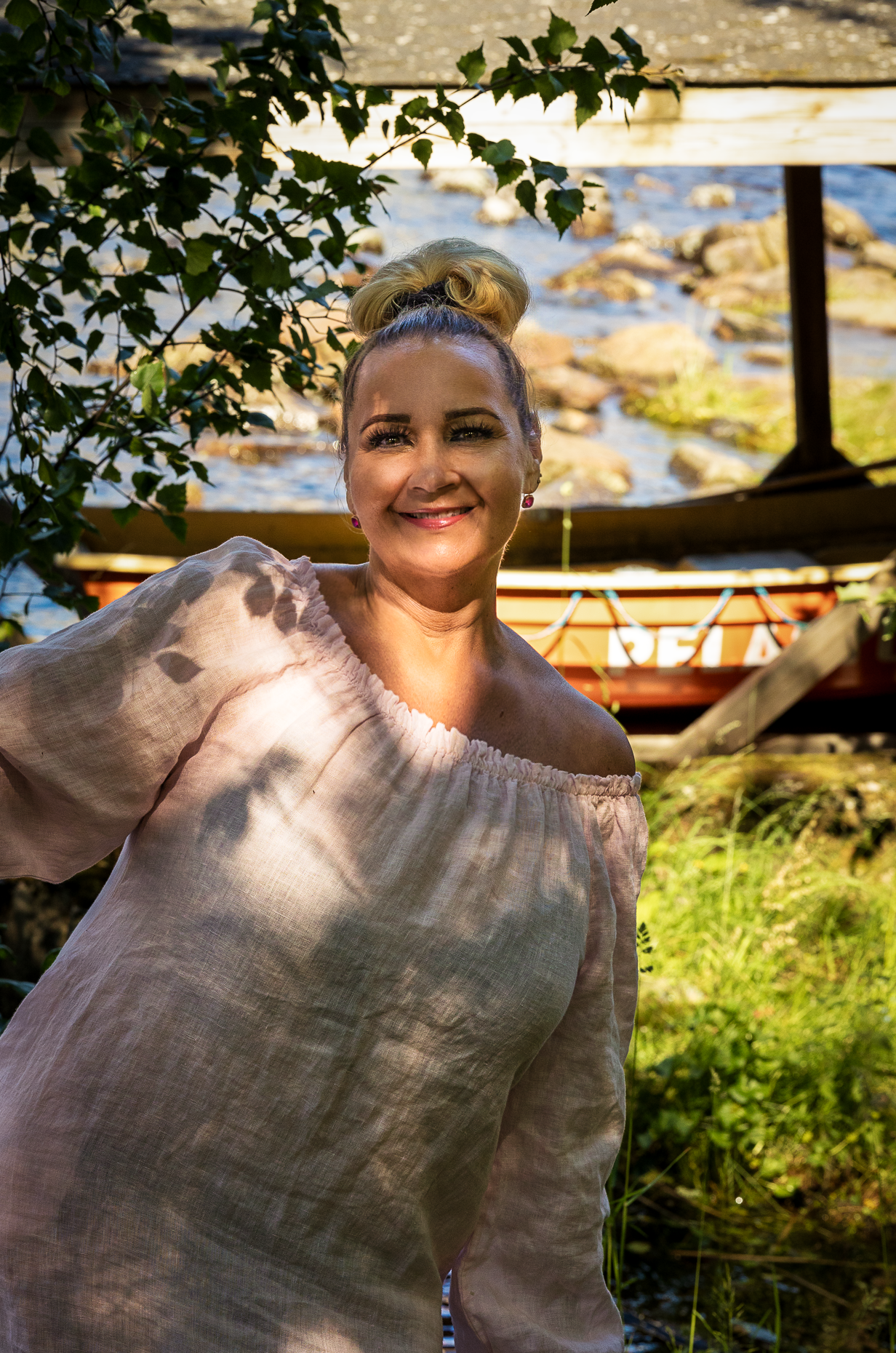 Erika seisoo hymyillen järven äärellä, taustalla pelastusvene