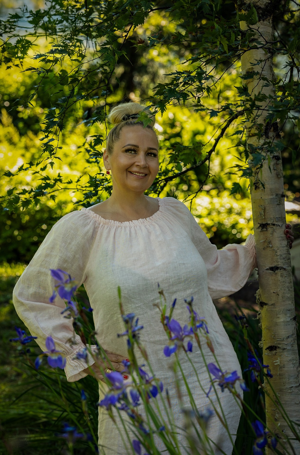 Erika seisoo kukkaniityllä, taustalla vihreä puutarha ja värikkäät kukat